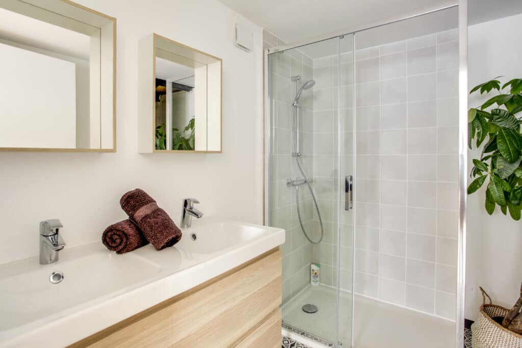 Salle de bain moderne : double vasque et douche Salle de bain moderne avec double vasque en céramique, robinetterie chromée, serviettes marron, et cabine de douche carrelée.